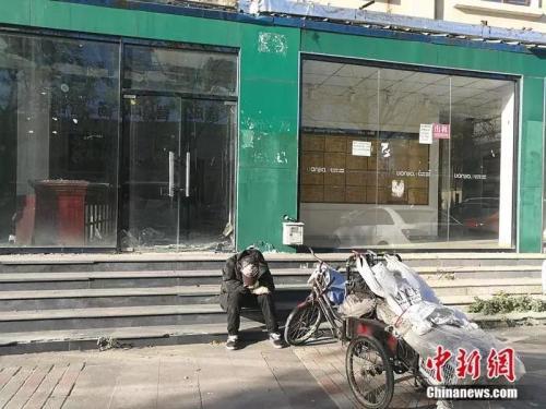 資料圖：2018年10月，燕郊“售樓一條街”，已經關門的鏈家門店前停著一輛裝貨的三輪車，車的主人坐在地上，把頭深深地埋進臂彎。